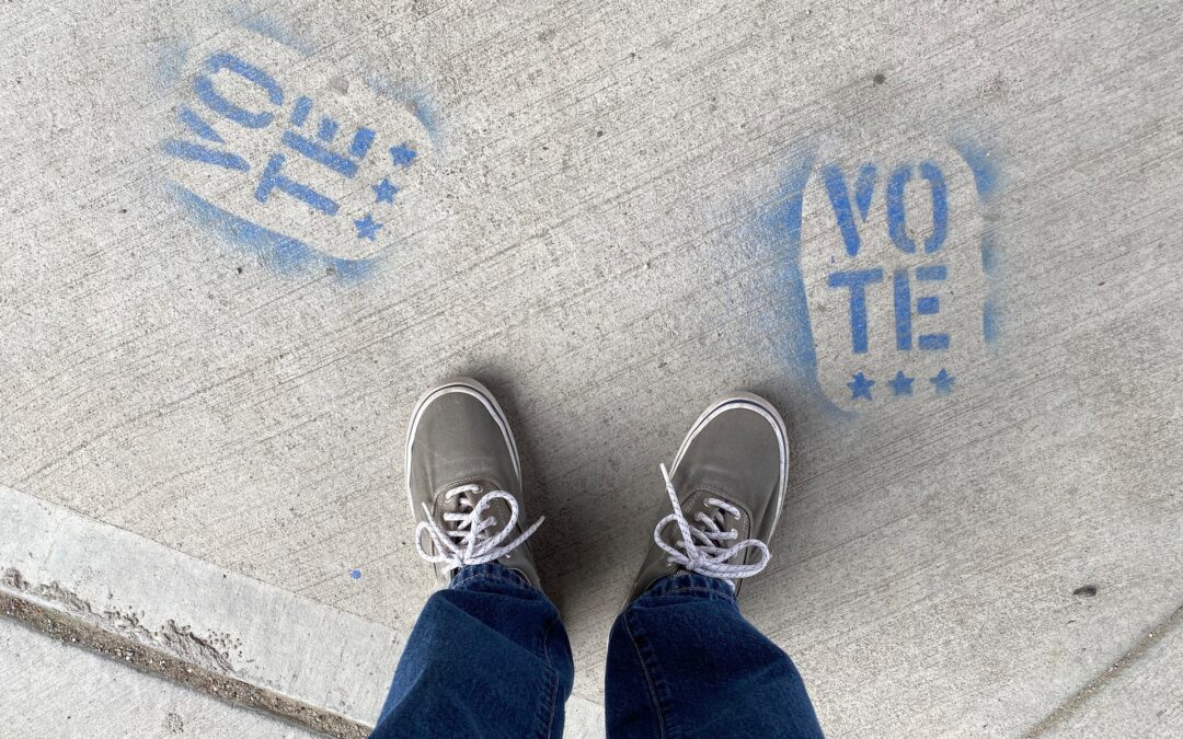 Side walk with the word "vote" written in chalk with a pair of grey and white sneaker in between