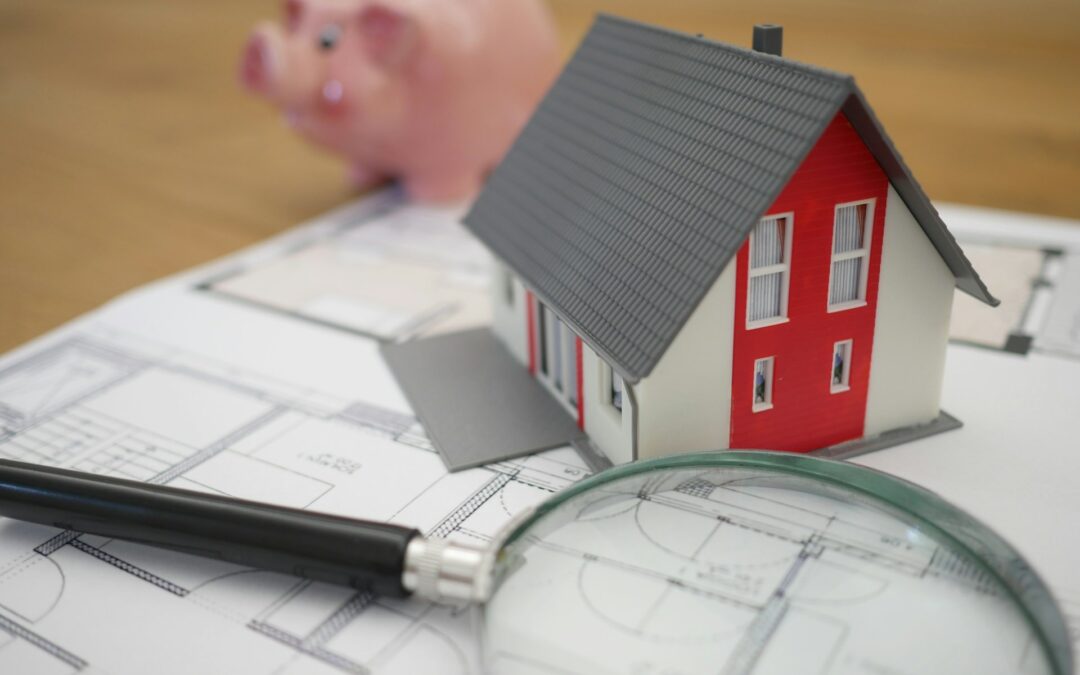 Red and white house figurine with a piggy bank, report and magnifying glass.